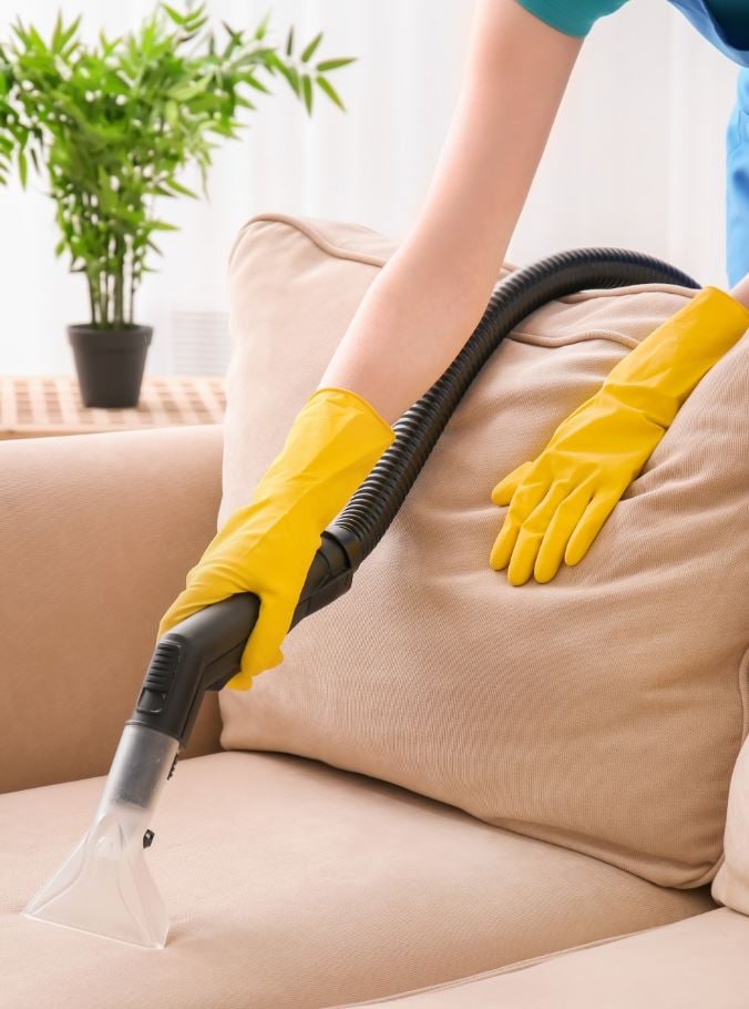 A woman in yellow gloves is doing an upholstery cleaning service​.